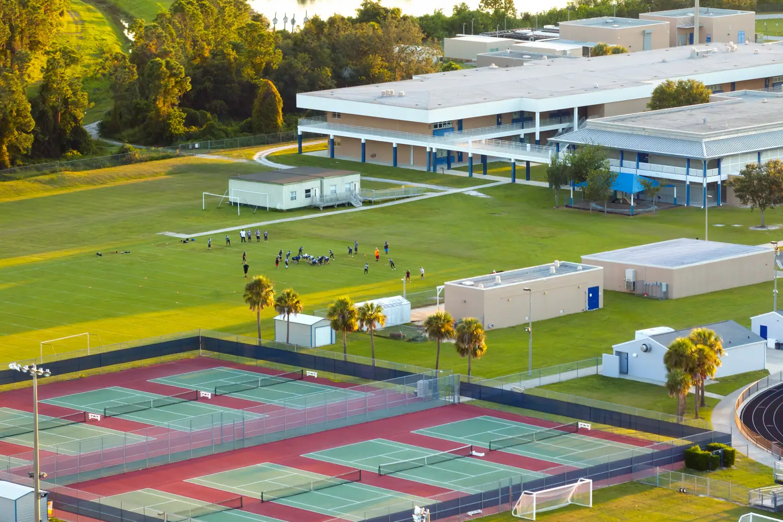 Aerial view of a school campus: tennis courts, playing fields and low classroom blocks among palms.