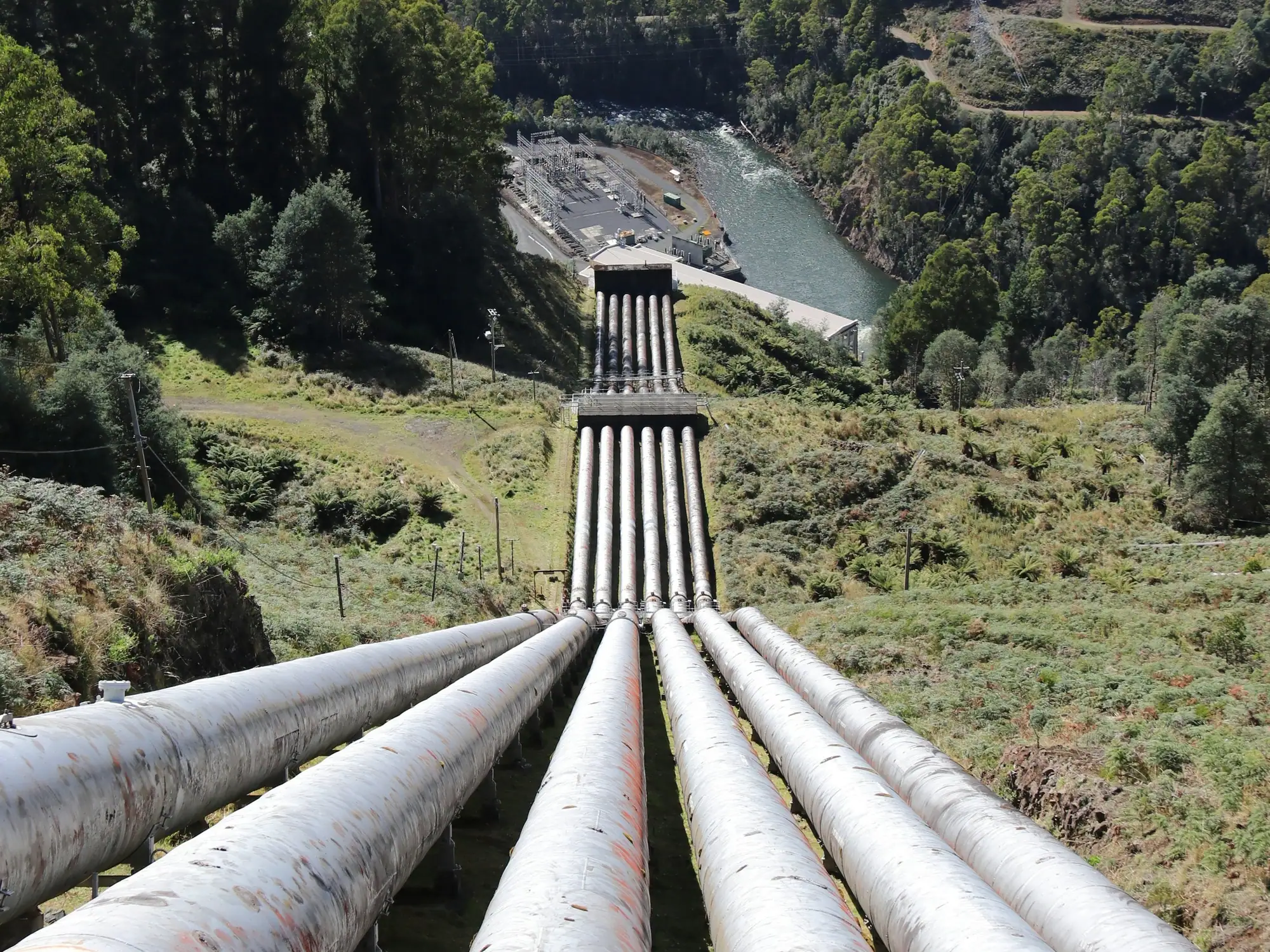 Hydro-electric penstock pipelines running down a forested hillside to a power station on the river below